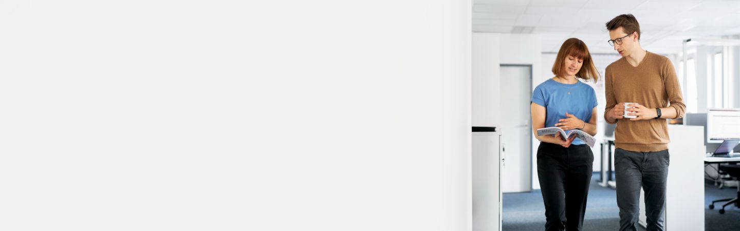  Двама колеги обсъждат в модерен офис как EOS може да защити компаниите от неплащане и да максимизира тяхната ликвидност в управлението на вземания, докато друг служител работи на компютъра на заден план.