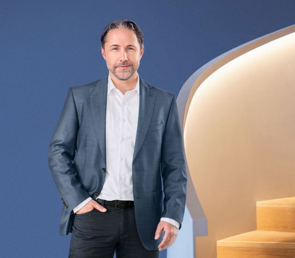 Марвин Рамке, главен изпълнителен директор на групата EOS, стои пред син фон, облечен в тъмно сако. Той гледа директно в камерата.