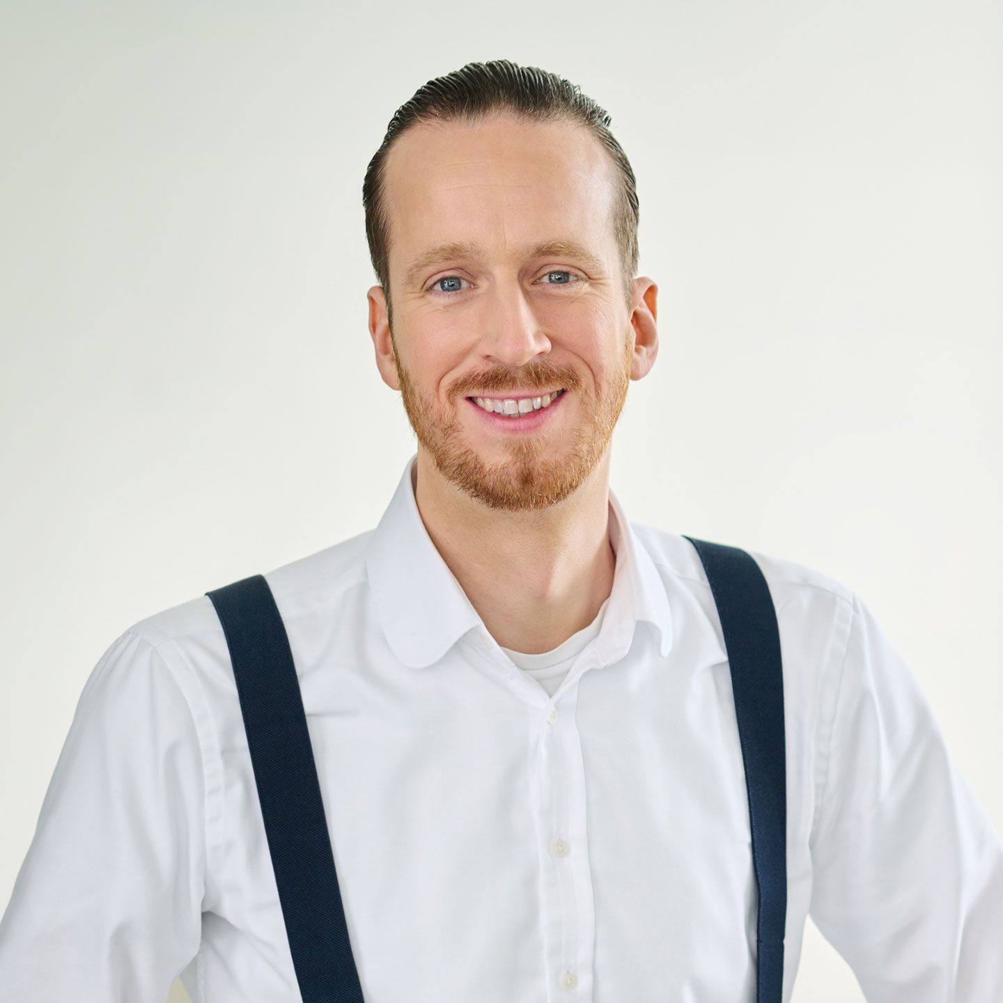 Portrait_2024_Sebastian_Pollmer Изпълнителен директор на групата EOS за Западна Европа Себастиан Полмер, мъж, в светло помещение, стои изправен с бяла риза и сини тиранти.