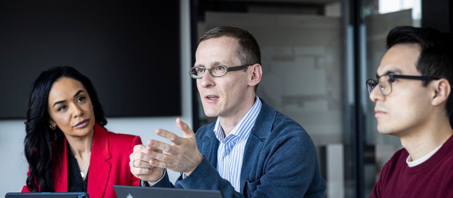 трима души разговарят в офис.